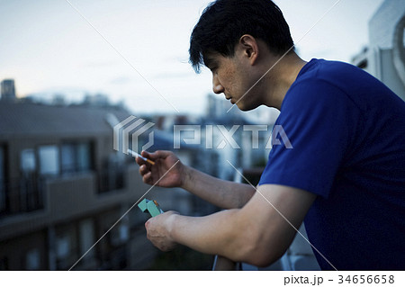 男性 一人 ベランダ タバコの写真素材