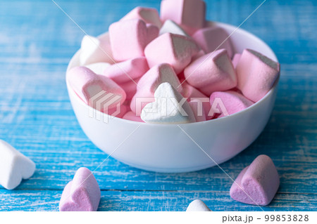 White and pink heart-shaped marshmallows are scattered from a cup